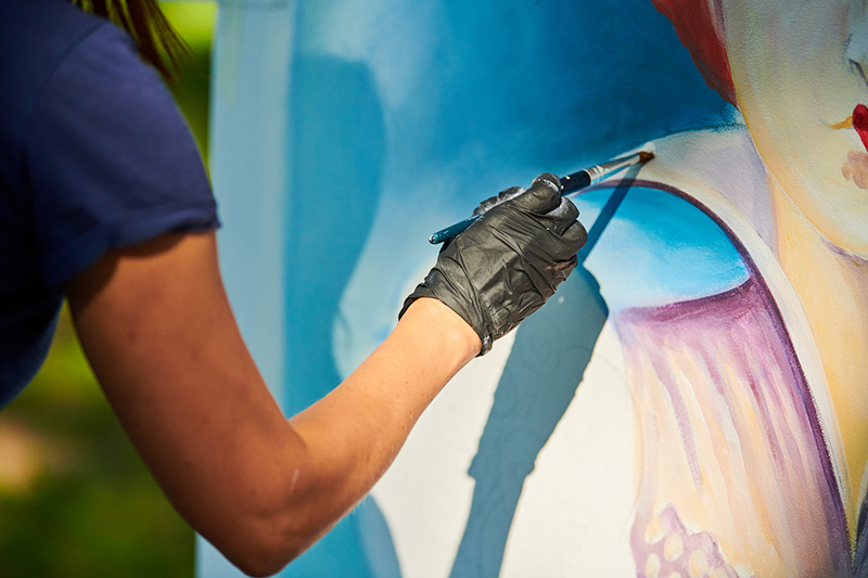 Girl artist hand holds paint brush and draws surreal fairy tale portrait on white canvas