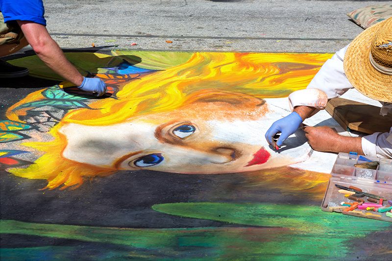 Two artists working on  chalk drawing at street art festival